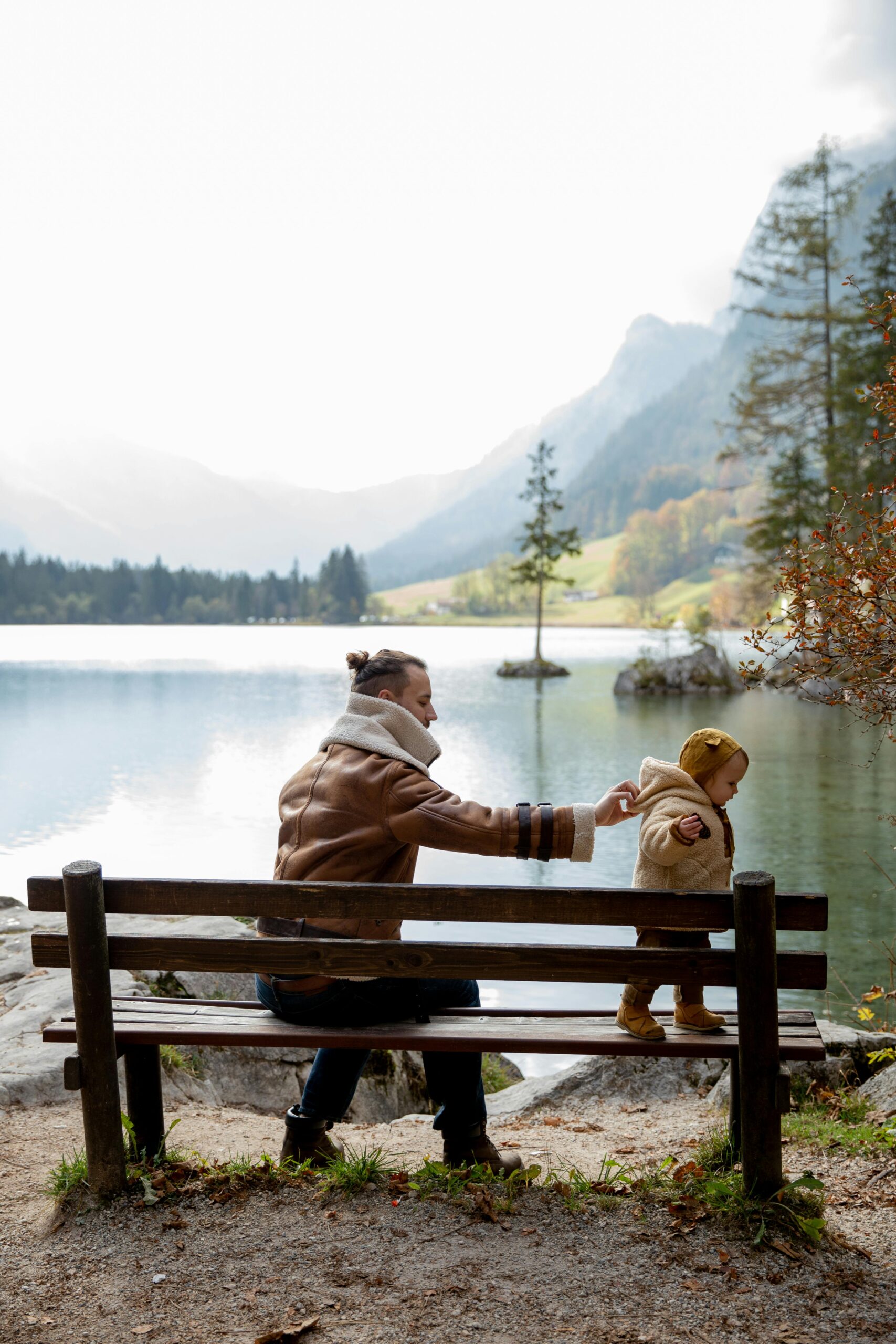 Father playing with child on a bench near a lake