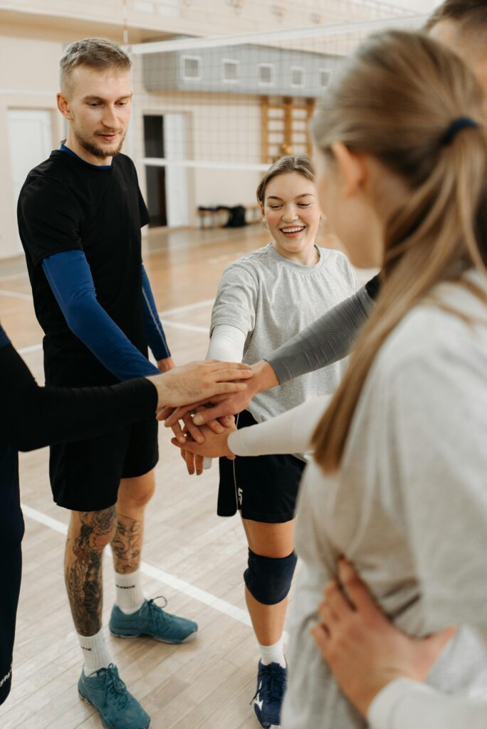 Group of volleyball players huddling and bringing their hands together after practice.