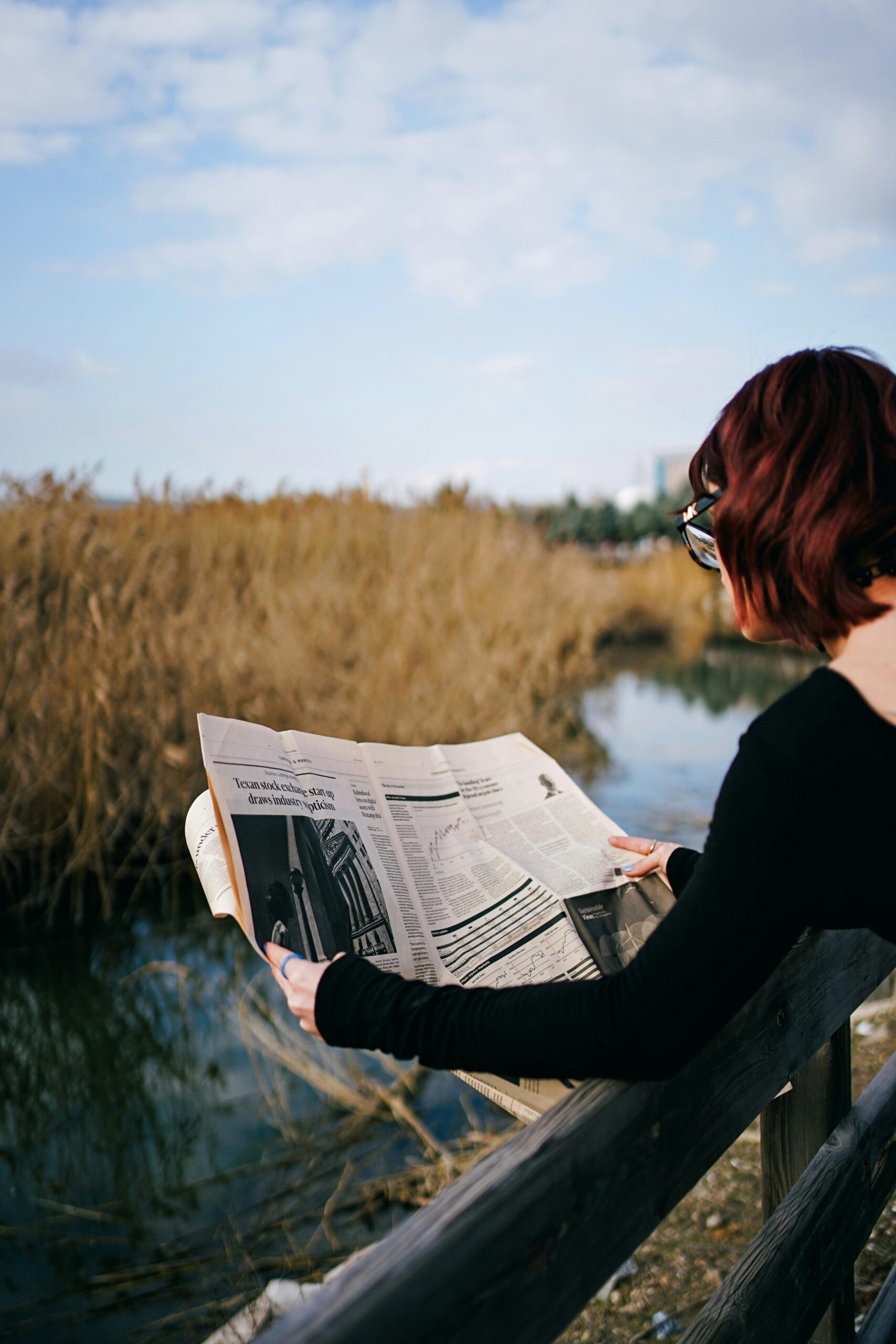 Woman reading newspaper while overlooking peaceful landscape