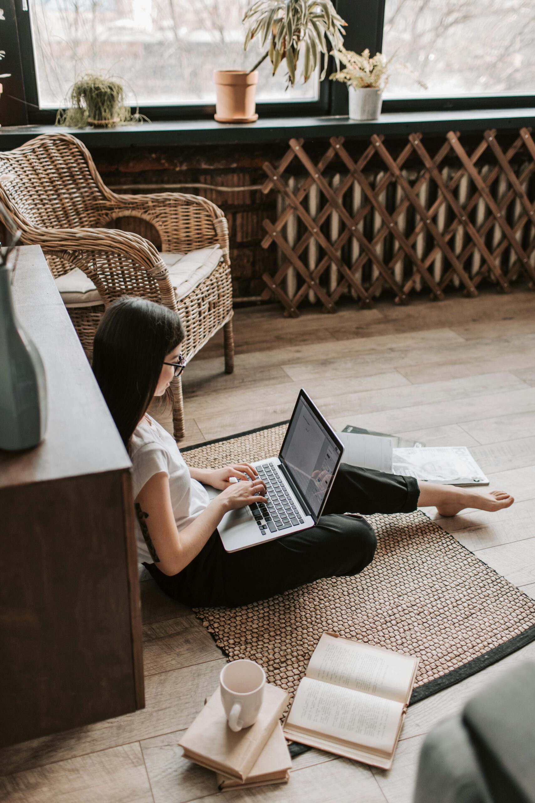 Woman sitting cross-legged on the floor, focused on her laptop screen