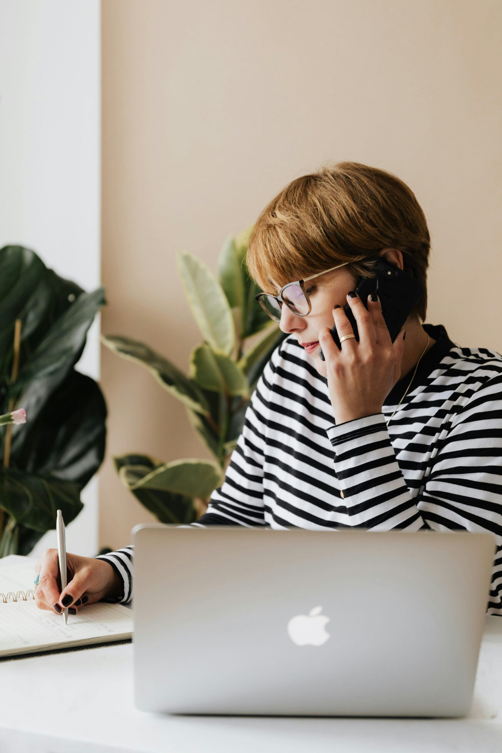 woman on her phone while working on laptop and taking notes