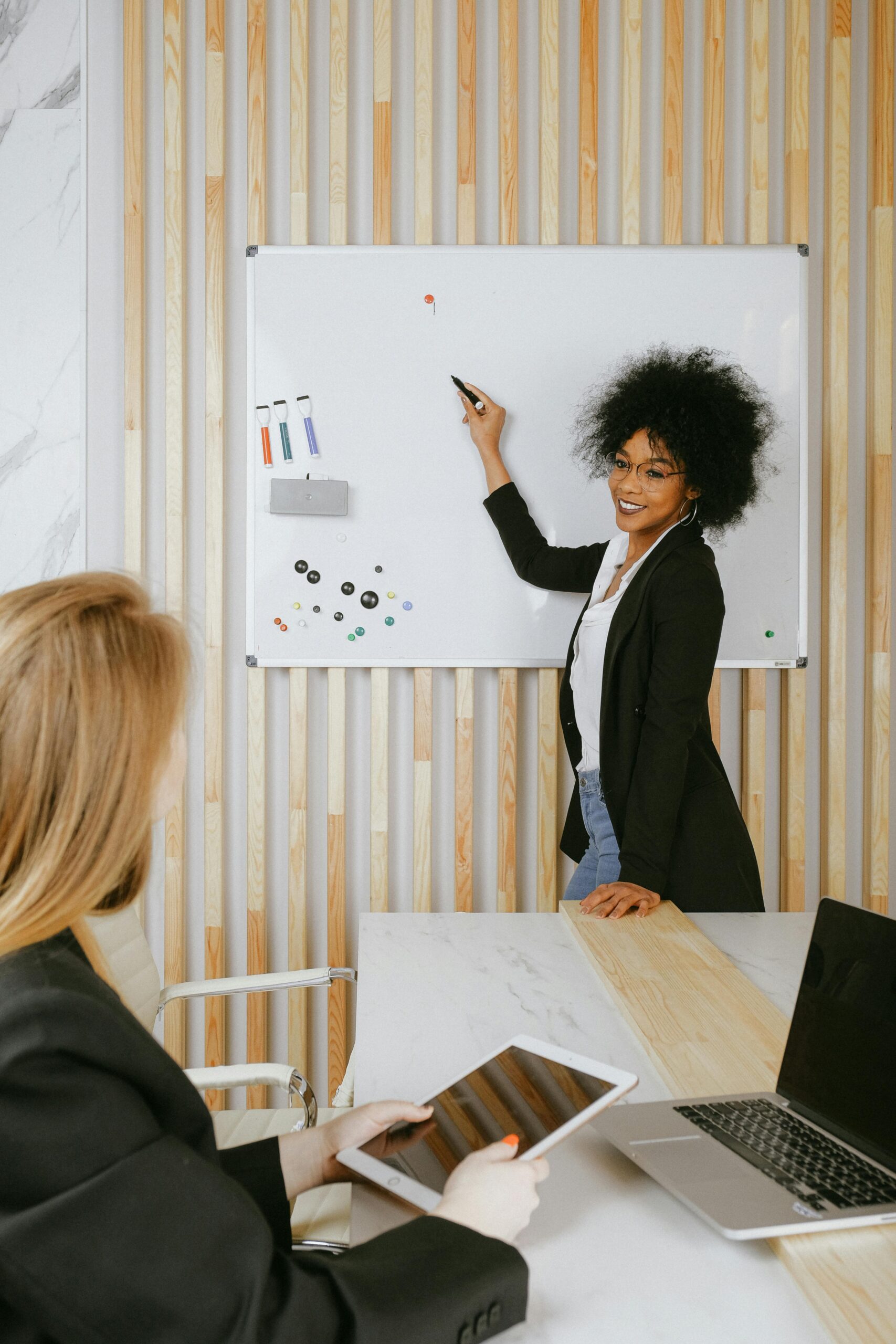 Woman using a whiteboardin a corporate meeting room while another woman listens