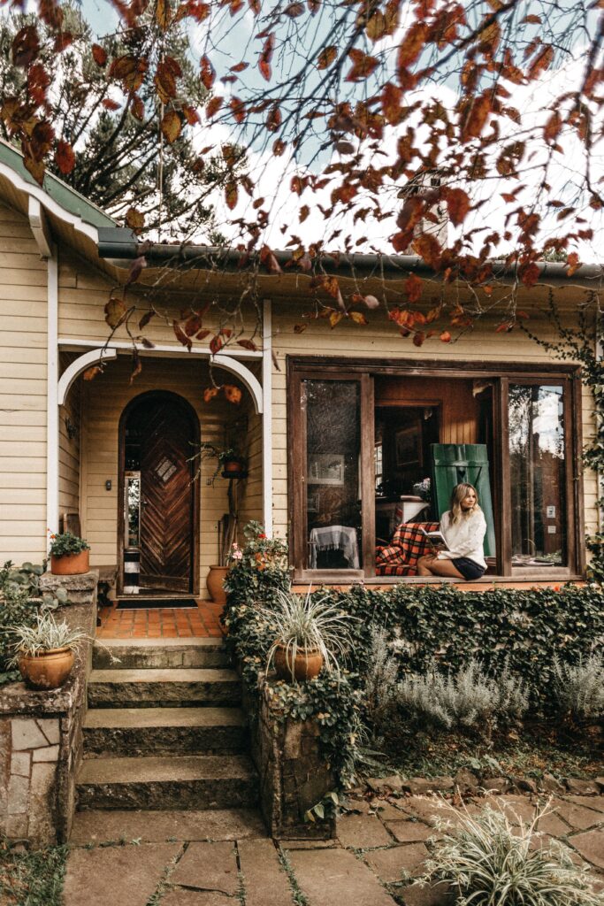 Charming bungalow with person relaxing on porch, surrounded by autumn leaves and greenery.